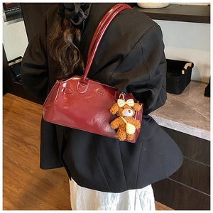 Macro shot of burgundy patent leather bag with brand logo and plush bear charm