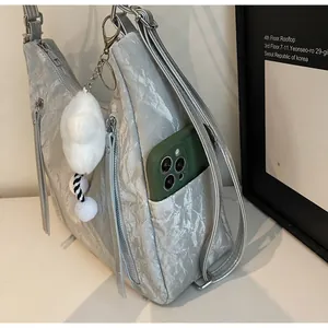 Detail of silver pleated bag showing side pocket, metal zipper and white plush charm