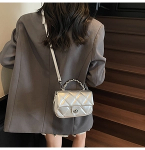 Sac à bandoulière matelassé argenté avec poignée chaîne porté sur un blazer gris