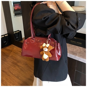 Detail of dark red patent leather shoulder bag with brand logo and cute plush bear charm