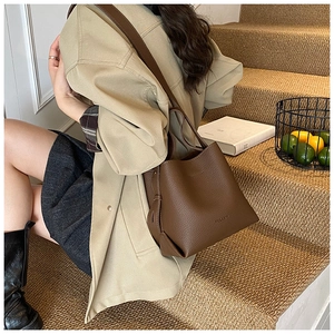 Détail d'un sac seau marron foncé en cuir grainé avec un trench-coat élégant