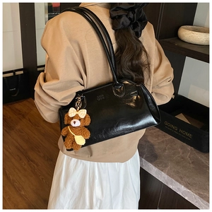 Detail of glossy black vintage oil-wax leather handbag with cute plush bear pendant accessory