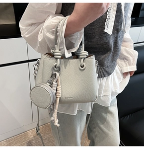 Dettaglio borsa in pelle litchi grigio chiaro con manico a nodo e ciondolo portamonete
