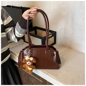 Detail of dark brown wax leather handbag with glossy finish and cute bear charm