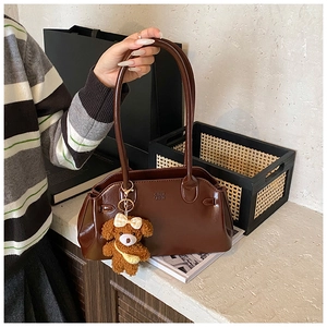 Close-up of brown oiled leather handbag with cute plush puppy charm and embossed logo