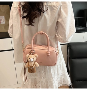 Detail of pink Boston bag with a teddy bear charm and adjustable shoulder strap