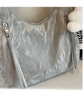 Close-up of silver wrinkled texture handbag with plush ball charm and tassel detail