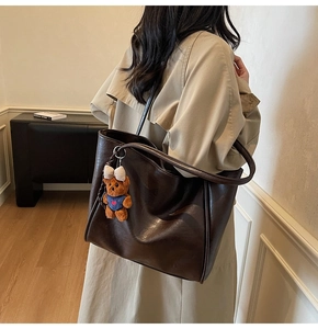 Deep brown tote bag detail with cute teddy bear charm on model's shoulder in interior