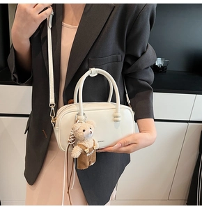 Detail of a beige crossbody bag with premium leather texture and a cute plush bear charm