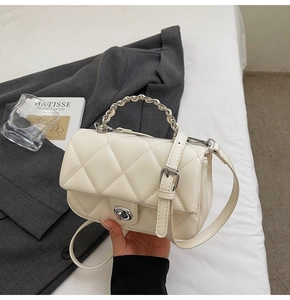Gros plan d'un sac crème matelassé avec fermoir rotatif argenté sur un blazer gris chic