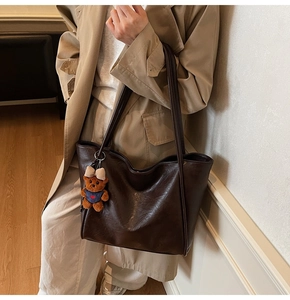 Detail of dark brown tote bag with bear charm on model in beige trench coat