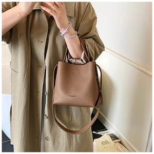 Détail du sac seau marron en cuir grainé avec logo embossé et bandoulière amovible
