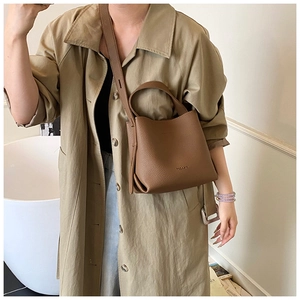 Sac seau marron en cuir grainé porté avec un trench pour un style élégant quotidien