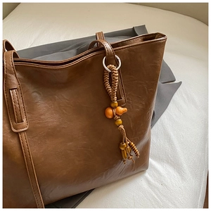 Detail of brown faux leather tote bag with vintage wood bead pendant on a grey suit jacket