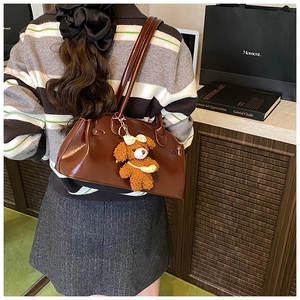 Detail of vintage oil-wax leather shoulder bag in caramel brown with teddy bear charm