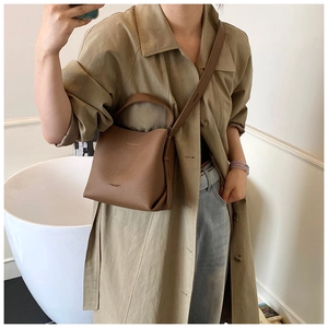 Sac seau en cuir grainé marron porté en bandoulière par un mannequin en trench-coat