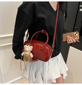 Detail of a dark red glossy Boston bag featuring a white logo and a cute bear charm