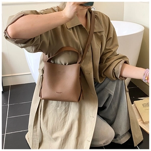 Détail du sac seau en cuir marron à motif litchi avec poignée ronde et bandoulière fine