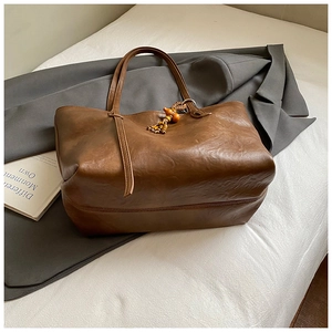 Brown vintage faux leather tote bag with wooden bead charm on a soft white bed sheet
