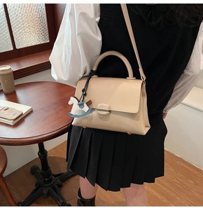 Sac fourre-tout en cuir beige avec serrure carrée et breloque cheval dans un décor de café