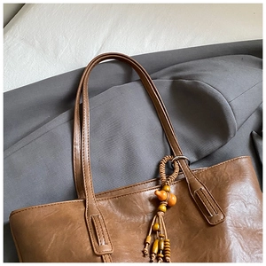 Detailed close-up of brown tote bag with ethnic wooden bead tassel and leather texture