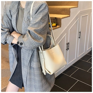 Détail du sac seau crème en cuir grainé avec logo doré et bandoulière amovible