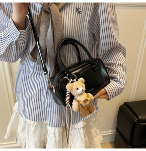 Close-up of black patent leather crossbody bag with a cute teddy bear charm pendant