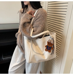 Close-up of white oversized tote bag with brown plush bear charm and pebbled texture