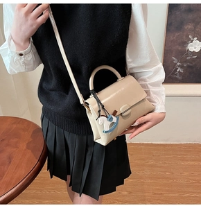 Détail du sac cabas en cuir beige avec breloque cheval bleu et bandoulière amovible