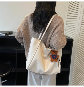 Close-up of white leather tote bag texture featuring a cute teddy bear charm pendant