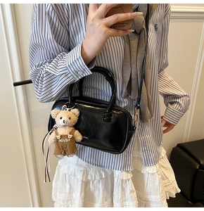 Detail of black glossy crossbody bag featuring white BAROK text and brown plush bear charm