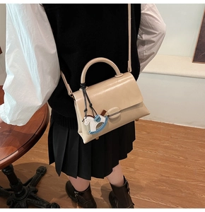 Détail d'un sac bandoulière crème en cuir souple avec un pendentif cheval élégant