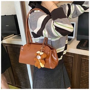 Close-up of brown oiled leather shoulder bag with plush bear charm and embossed logo