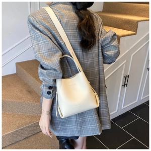 Détail du sac seau en cuir grainé beige montrant la texture et la bandoulière ajustée