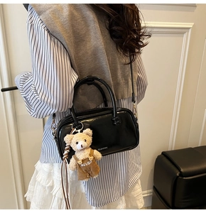 Detail of black glossy handbag with CLEAROK text and teddy bear charm on model