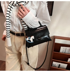 Détail d'un sac cabas en cuir verni noir avec un charm cheval à bascule sur un mannequin
