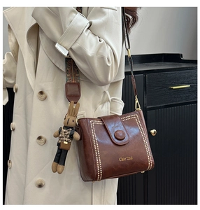 Detail of vintage brown leather bucket bag with gold rivets and ethnic woven shoulder strap