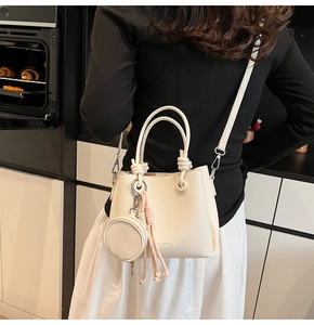 Dettaglio borsa tote beige con trama martellata, mini pochette rotonda e nappa decorativa
