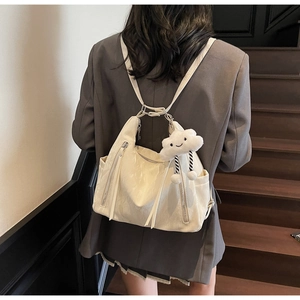 Rear view of a white multi-purpose backpack featuring a plush cloud charm on dark stairs