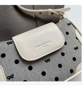 Close-up of grey herringbone fabric shoulder bag with black polka dots and leather pocket