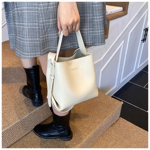 Gros plan d'un sac seau blanc crème en cuir grainé lychee tenu par un mannequin