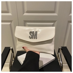 Detailed view of a white patent leather envelope clutch featuring a large rhinestone SM logo