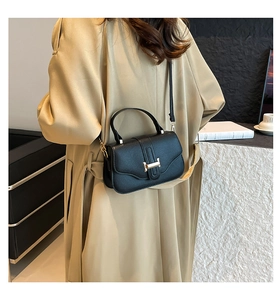 Borsa a tracolla in pelle nera con fibbia dorata indossata su un trench beige classico