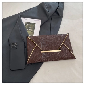 Close-up of brown snake-skin envelope clutch with gold metal trim on a stylish background