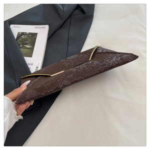Detail of dark brown snake-embossed clutch bag with gold metallic edge accent