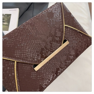 Macro shot of dark brown snakeskin texture and golden metal buckle on envelope clutch bag