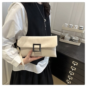 Detail of a chic cream underarm bag with a bold black square buckle and wristlet strap