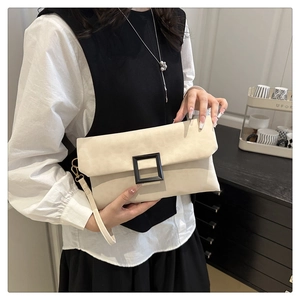 Detail view of a cream envelope clutch bag with a large black square buckle and wrist strap