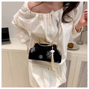 Close-up of black velvet crossbody bag with white floral embroidery and gold tassels