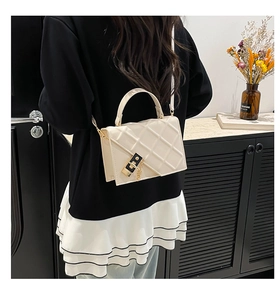 Detail of a beige quilted crossbody bag with gold hardware and top handle design